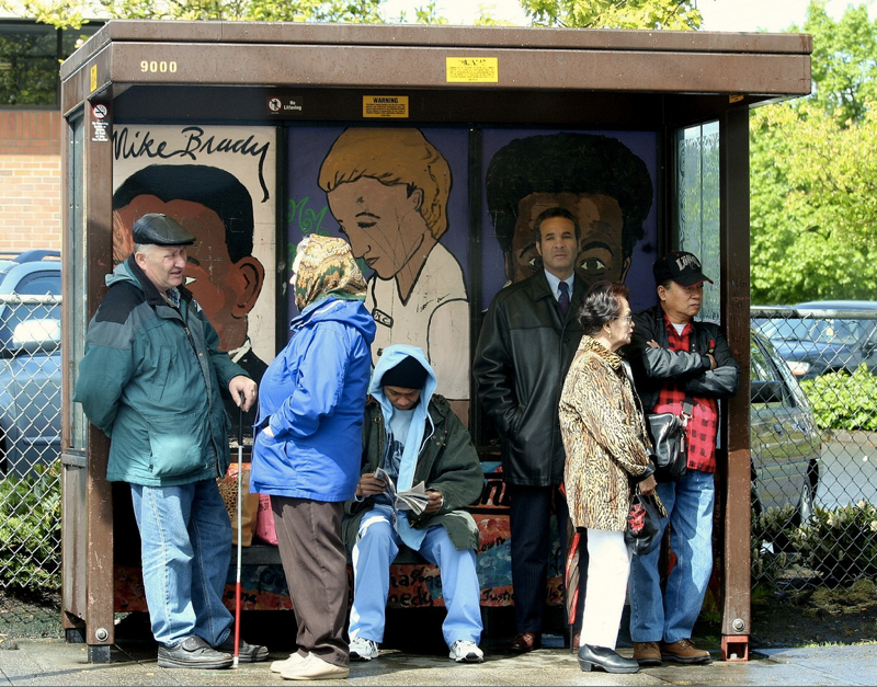 A packed bus stop shelter with several elderly people waiting.