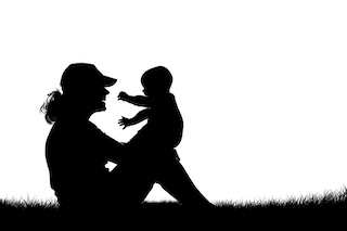 Stock photo of a silhouette of a mother holding a baby in the park.