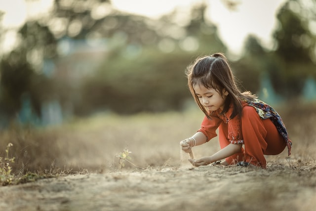 A photograph of a small child kneeling, playing with sand