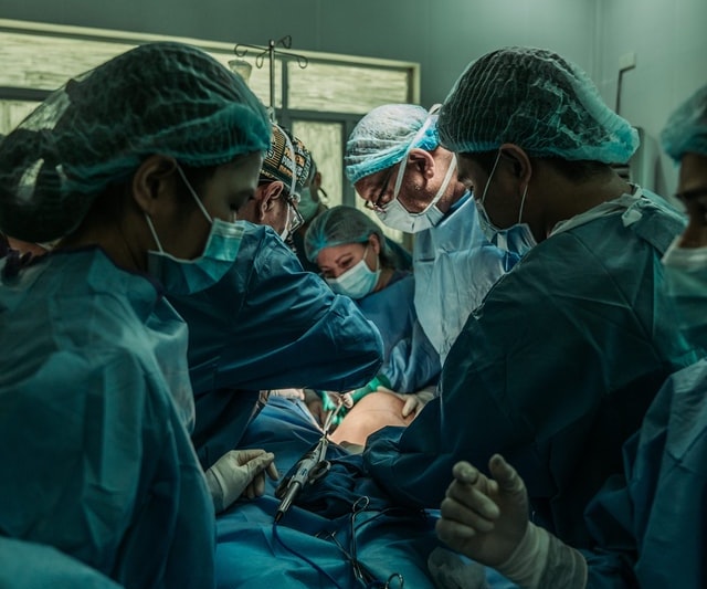 A photo of a surgery with five surgeons and nurses