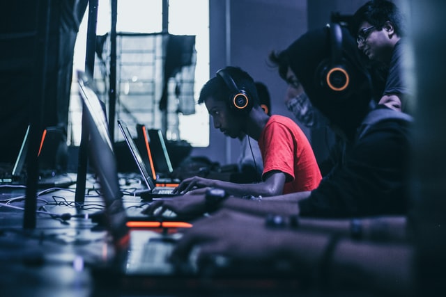 A photograph of people gaming in front of PCs in the dark