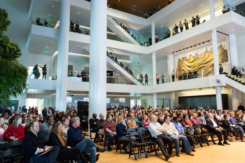 A photograph of a Bill & Melinda Gates Foundation company meeting, showing hundreds of people on three stories listening to a speaker