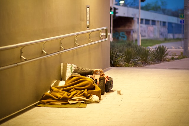 A man laying on the sidewalk under a blanket.