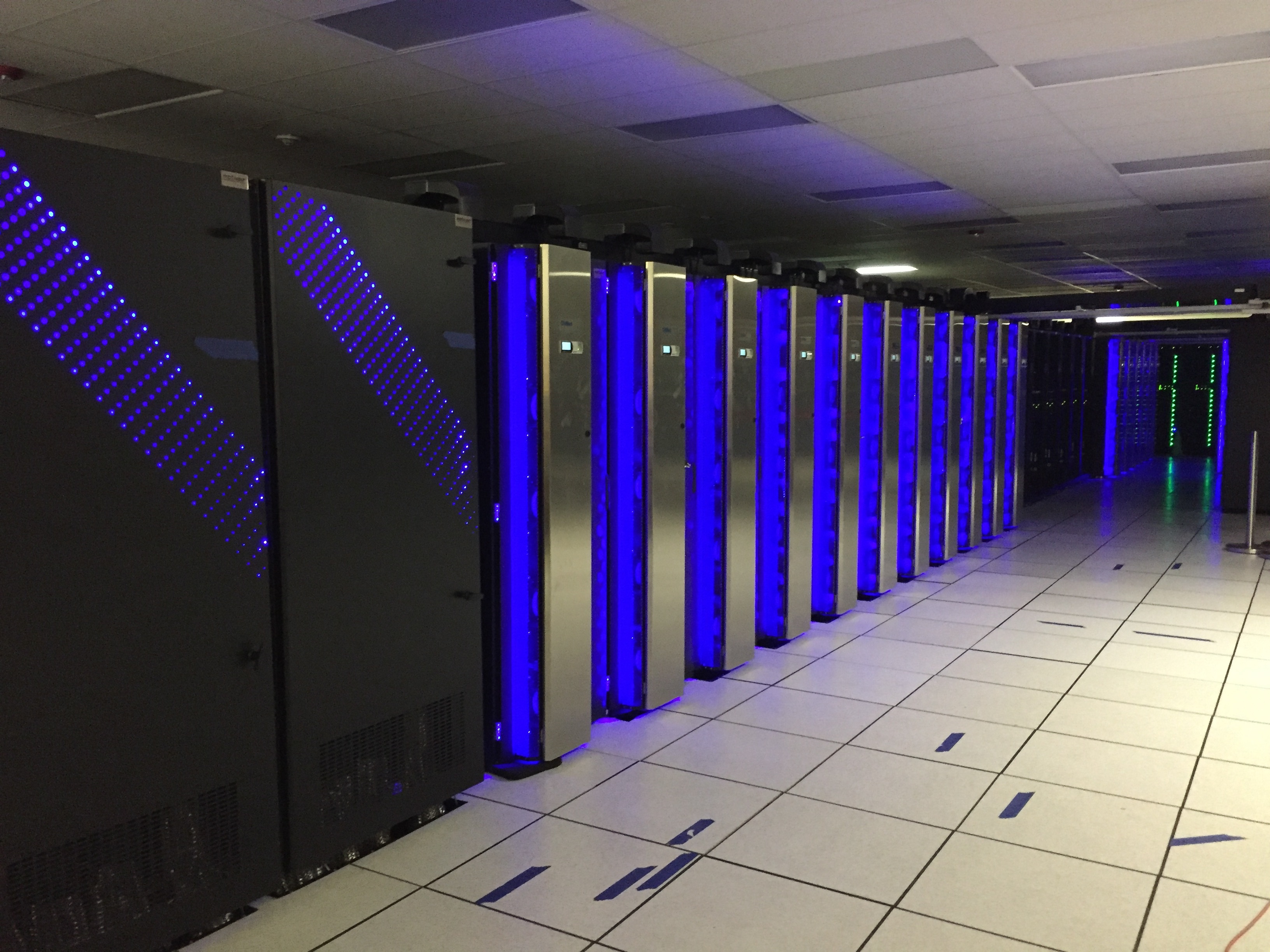 A photograph of rows of black and blue servers in an empty hallway.