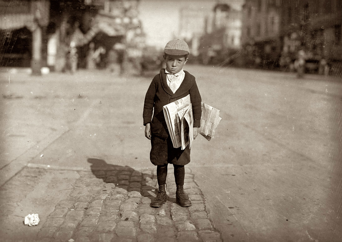 A 1915 photograph of a newsboy carrying some newspapers for sale