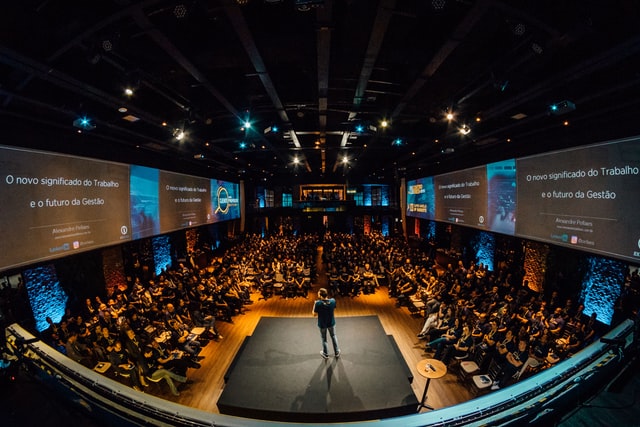 A photograph of a person speaking to a large audience