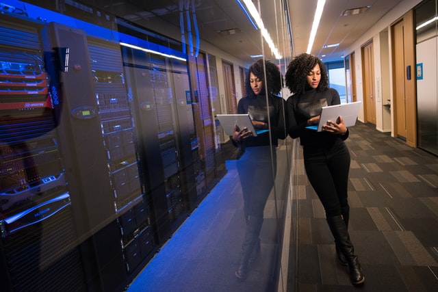 A photograph of a woman standing next to a row of servers in a data center