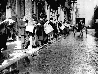 A black and white white photograph of a row of men reading newspapers on the sidewalk
