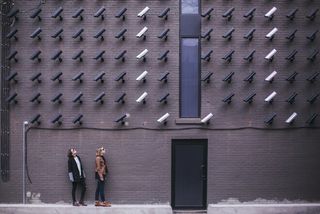 Two women look up to a wall of surveillance cameras
