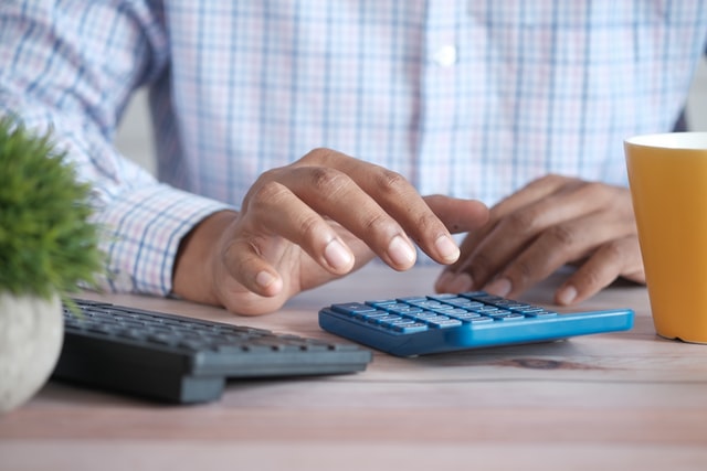 A person at a desk about to use a basic calculator.