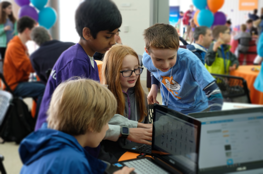 Four children standing around a laptop writing Scratch code.