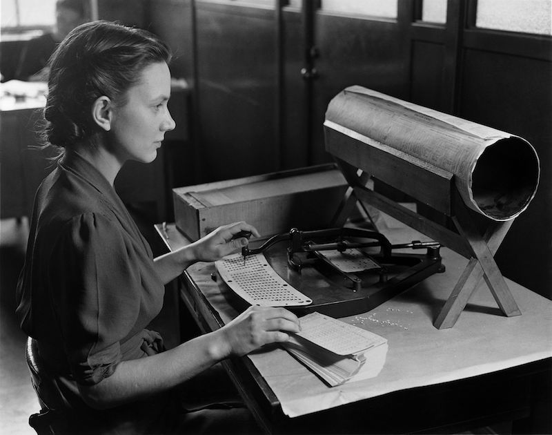 A photograph of a woman using a punchcard machine.