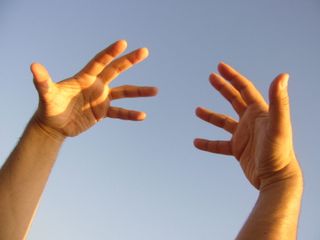 Two human hands in the sun facing a blue sky