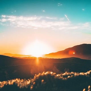 A sunrise, or possibly a sunset, over silhouettes of hills.