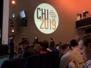 A photograph of the CHI 2019 plenary showing a few attendees waiting for the keynote to start.