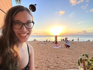 Amy smiling with her hair down with a sunset and beach in the background.