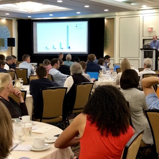 A photograph of the ICER 2019 audience, sitting around round tables.