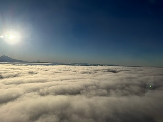 A muted, fuzzy photo above the clouds, with the bright sun in the corner, possibly from an airplane window.