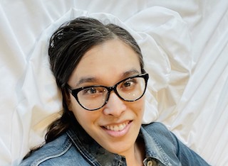 Amy laying on white sheet, smiling at the camera.