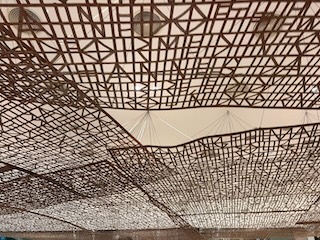 wood latices hanging from the ceiling of a beige foyer.