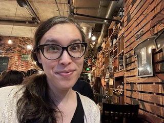 Amy smiling at the camera with a backdrop of eclectic objects in a restaurant.