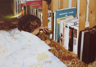 A photograph of Amy as an infant reaching for books on a bookshelf.