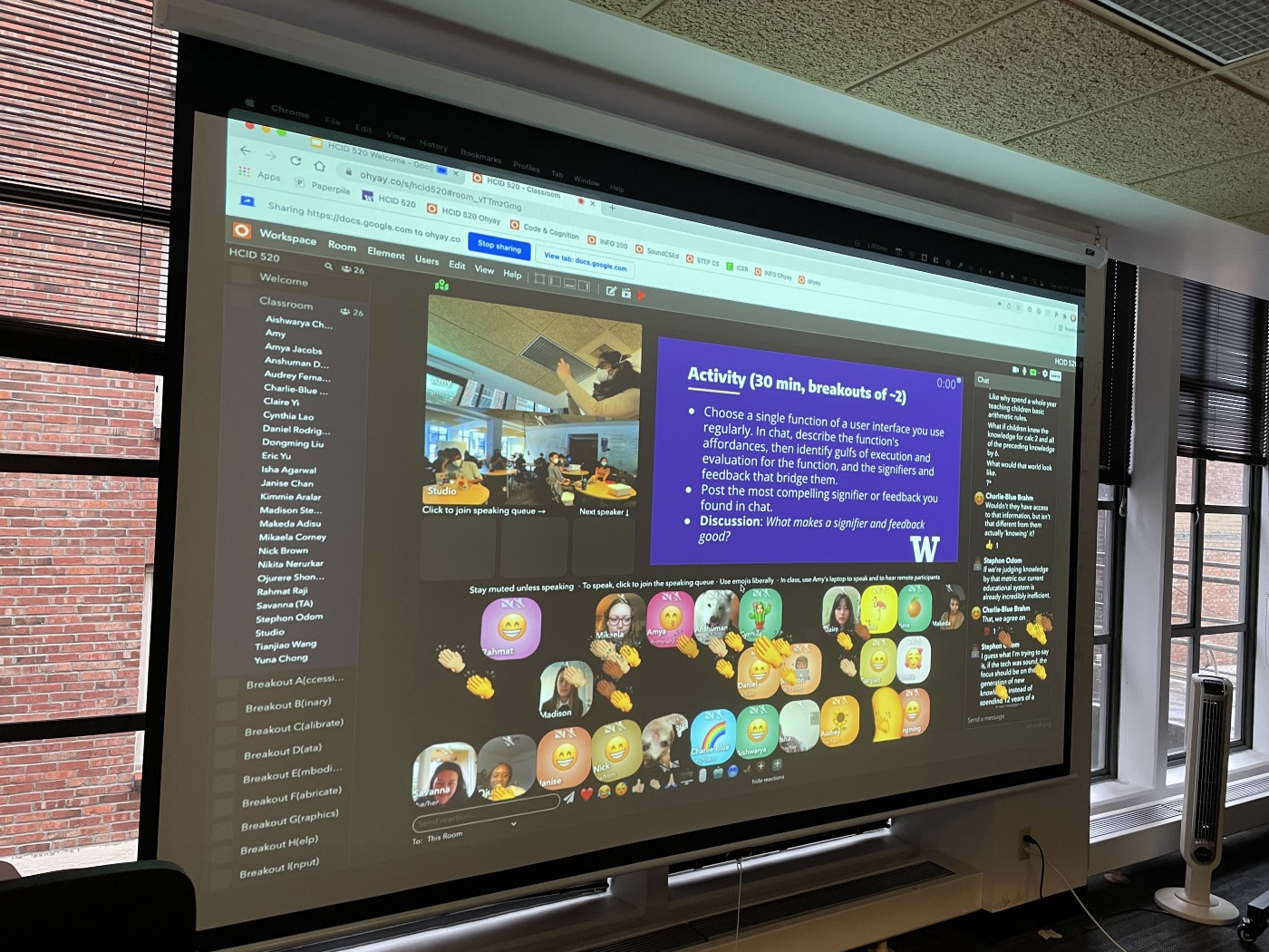 A photograph of a projector screen showing an Ohyay virtual classroom and several video feeds.