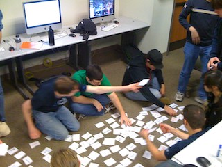 A photograph of students sorting notecards on the ground.