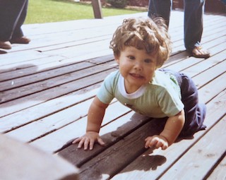 9 month old Amy smiling and crawling on a wooden deck.