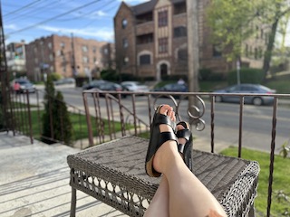 A street, a porch, an outdoor ottoman, and Amy's legs wearing black Birkenstocks. The sun shines and the first perspective suggests calm.