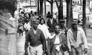 Twenty Black residents of Montgomery Alabama walking on a sidewalk in 1955.
