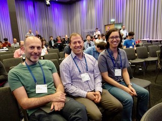 A photograph of me sitting next to two Andy's at a conference.
