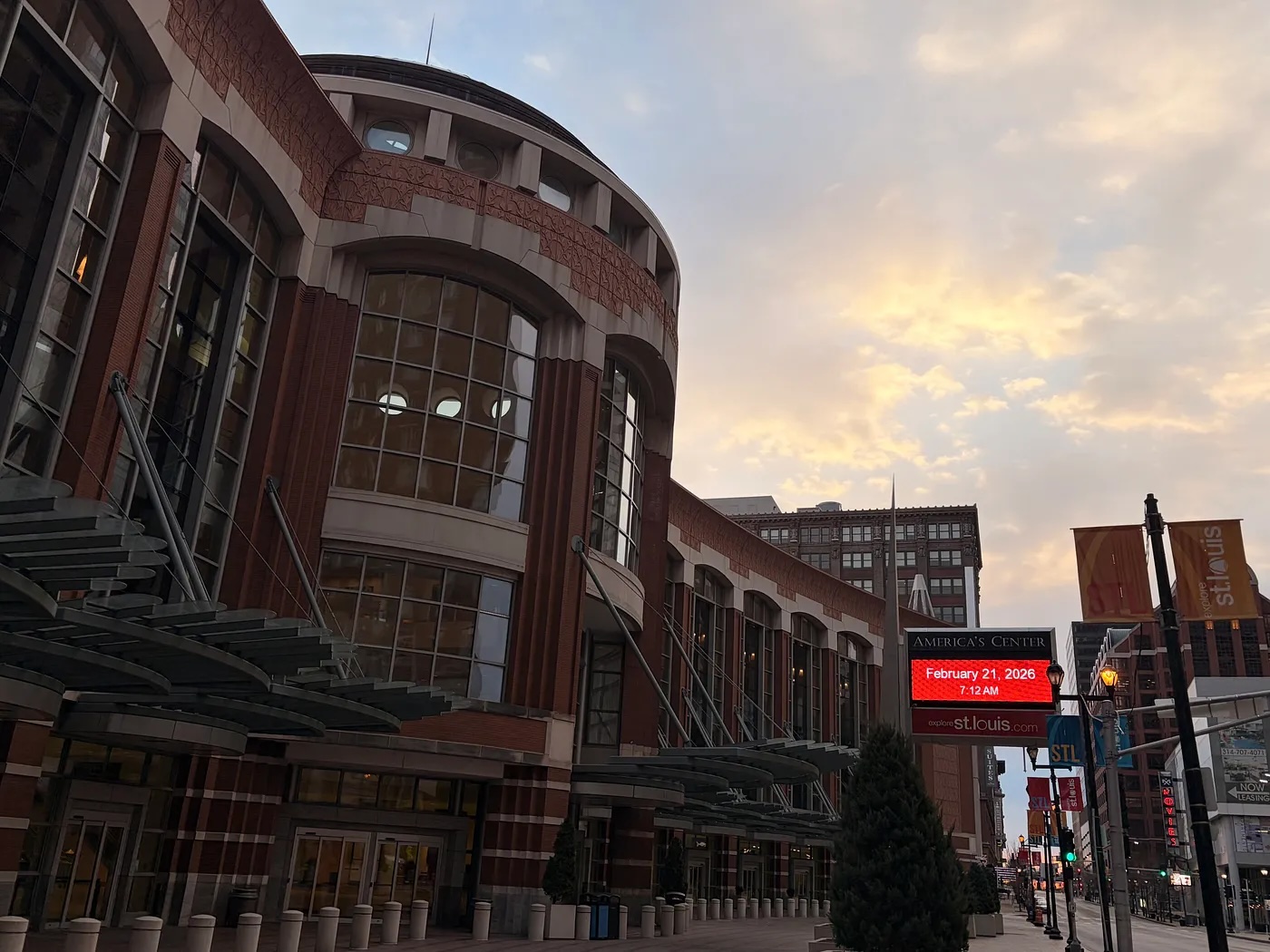 A brick, circular, windowed facade against a cloudy, sunny morning dawn.