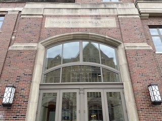 A brick entrance with glass doors and a sign etched Joan and Sanford Weill Hall.