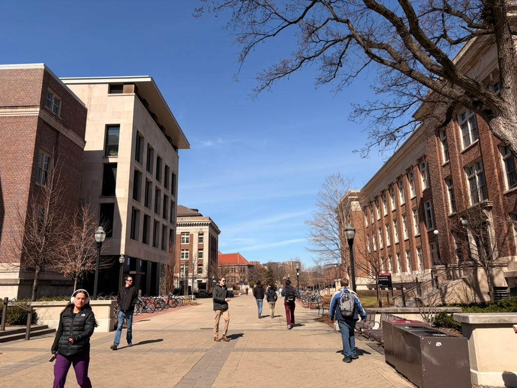 Brick buildings on the left and right, a handful of students walking down a pathway, and blue skies.