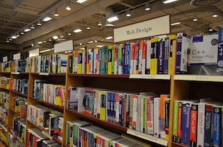 A photograph of a bookshelf of technical books for learning to code.