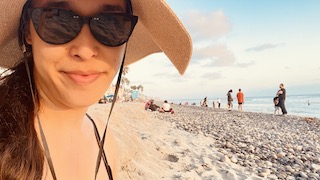 Amy in sunglasses, a sun cat, against a backdrop of sand, waves, and blue skies.